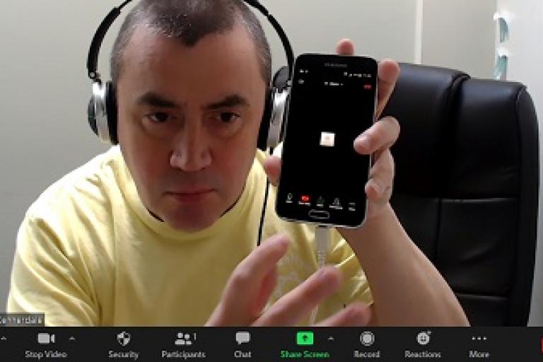 screenshot from a zoom call, with a man showing his smartphone to the screen