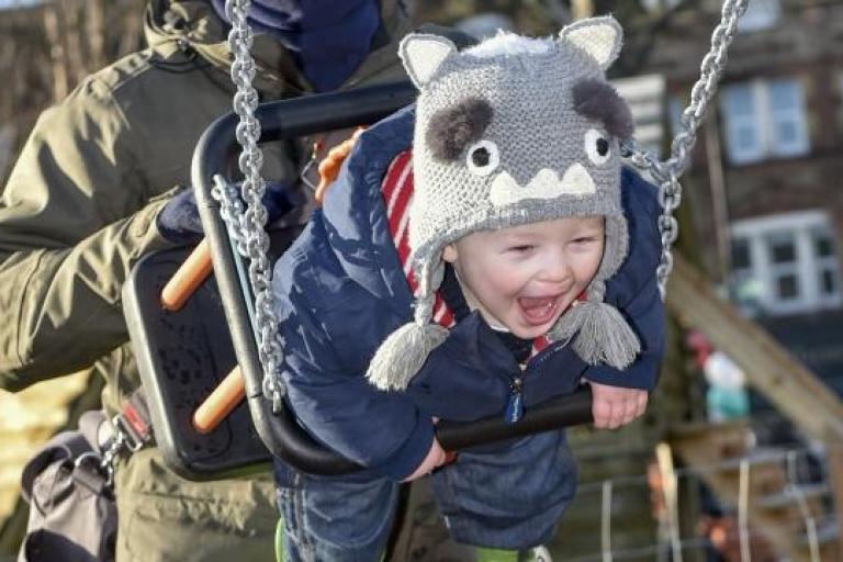 A father pushes an excitable toddler on a swing 