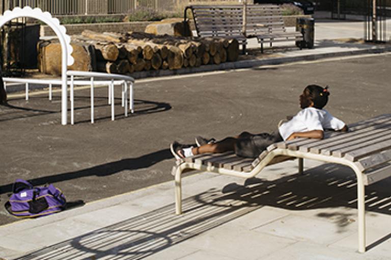 a child sat on an unusually shaped bench with a gently angled back that forms part of a second spot that you could sit on