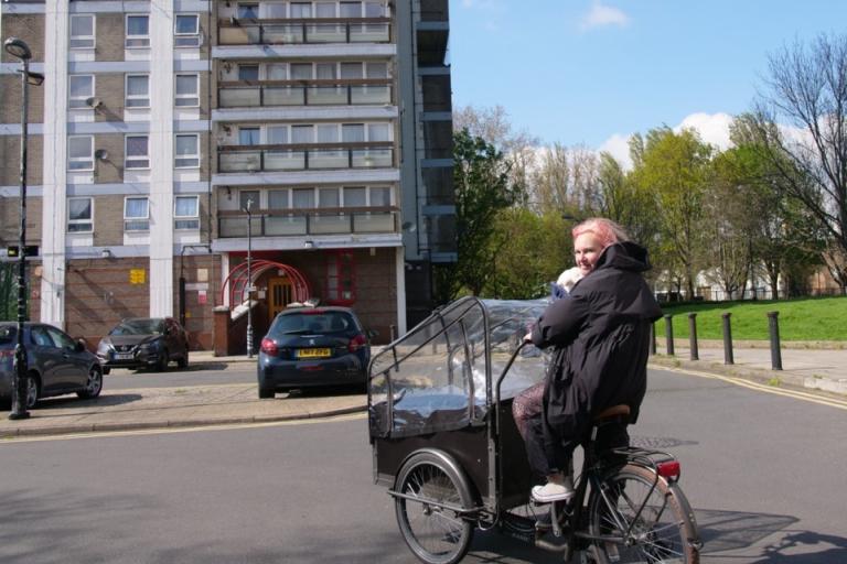 Woman with pink hair cycling through an estate on a cargo bike