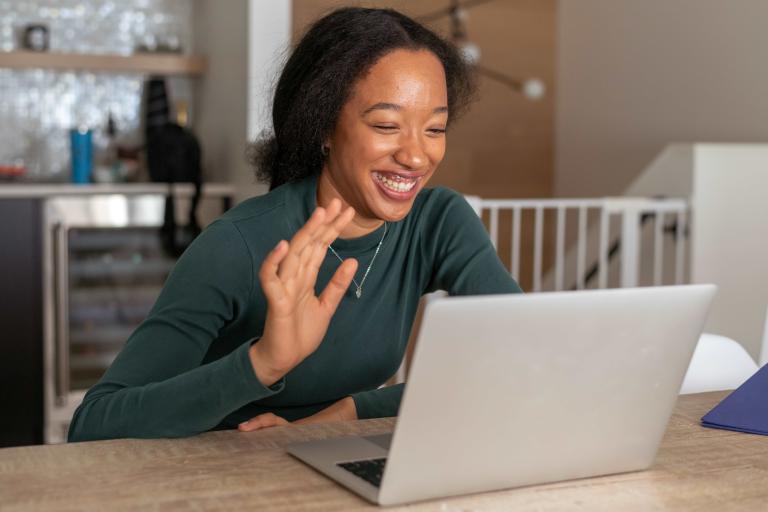 Woman waving and smiling at laptop screen