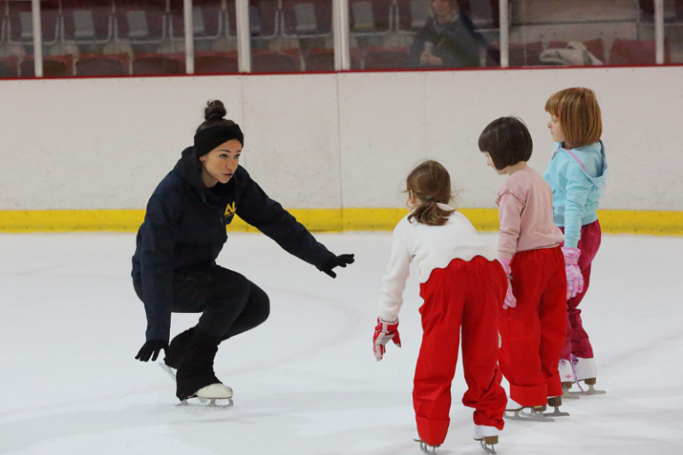 A female ice skating instructor on the ice with three children  