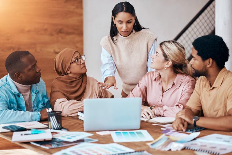 A group of people around a desk with a shared laptop in the middle