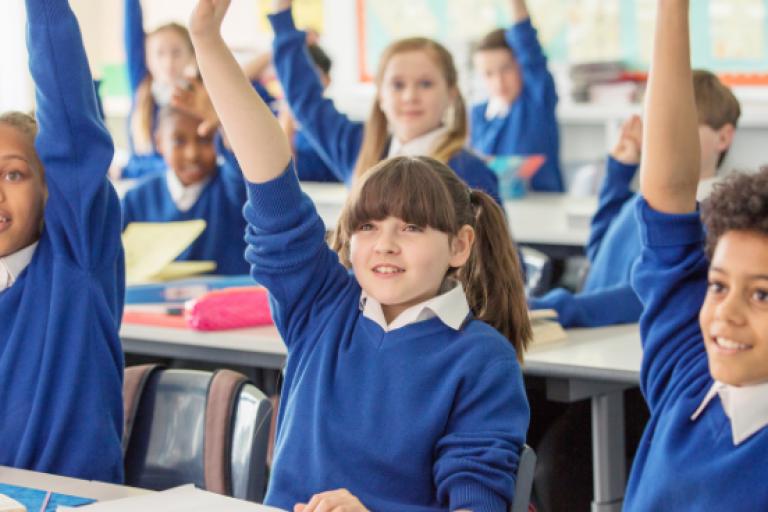 Pupils in classroom with hands up
