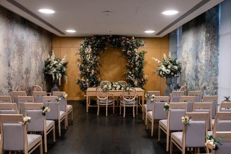 Olive Morris Room set up for a wedding ceremony with a floral arch, ceremony table and guest seating.