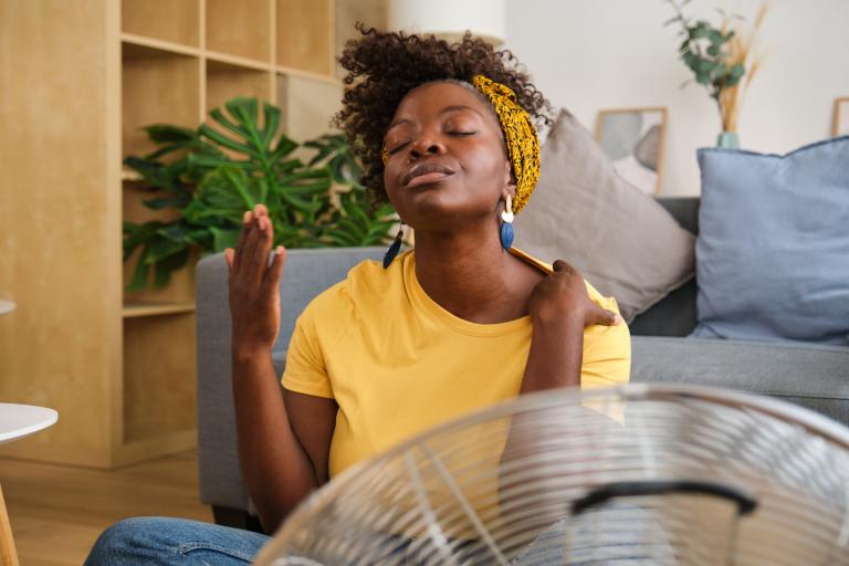 Girl sits in front of fan to cool down