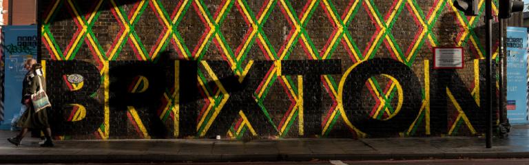 Artist painted Brixton in black and a mixed colour border on a wall under Brixton Rail bridge