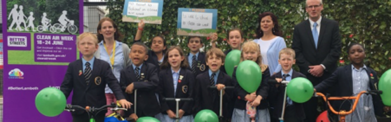 Councillor Claire Holland joins primary school pupils and teachers outside of Lambeth primary school entrance with green leaves on school fence to protect from air pollution