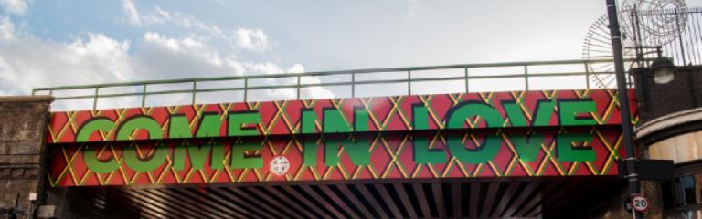 Come in Love artist painting on rail bridge in Brixton