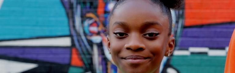 Girl smiling at camera in front of grafitti wall