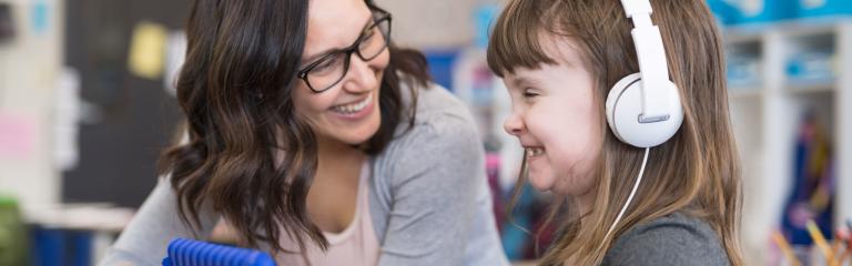 Woman showing information a tablet to a child wearing headphones