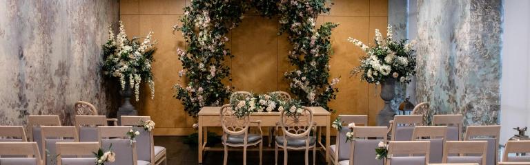 Olive Morris Room set up for a wedding ceremony with a floral arch, ceremony table and guest seating.
