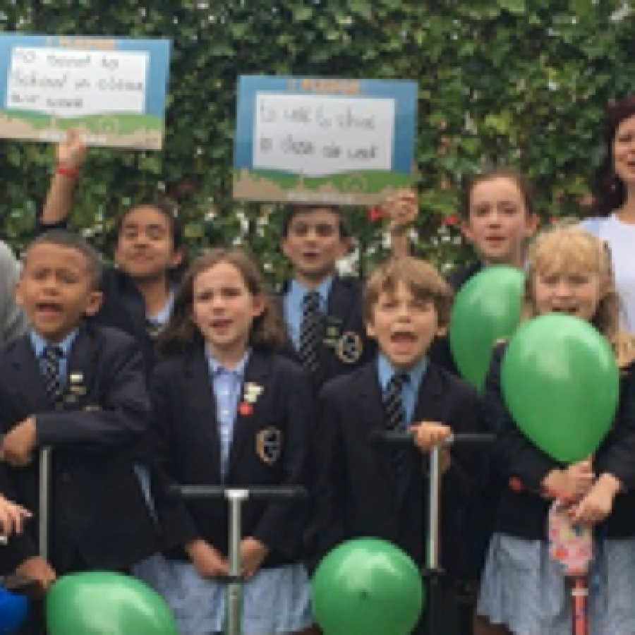 Councillor Claire Holland joins primary school pupils and teachers outside of Lambeth primary school entrance with green leaves on school fence to protect from air pollution