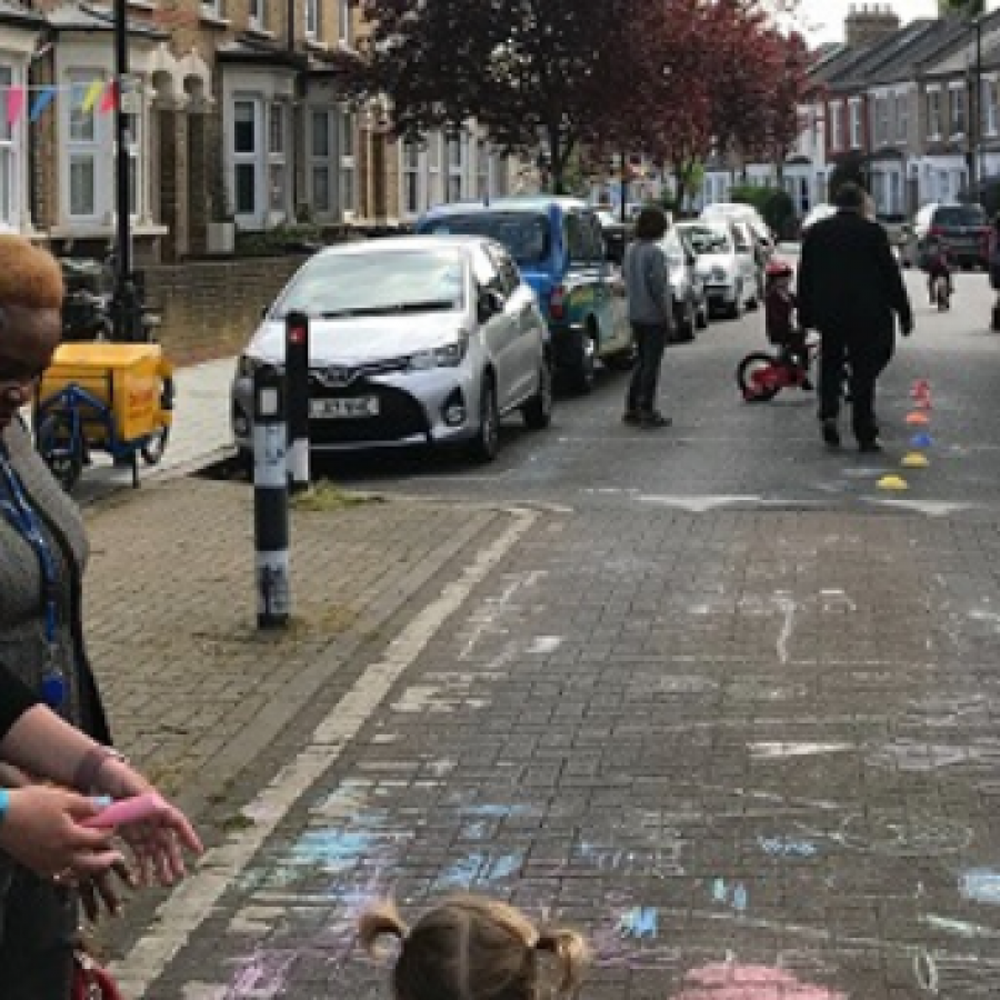 children and their parents on a closed road. Children are playing and using to coloured chalk to draw on the ground