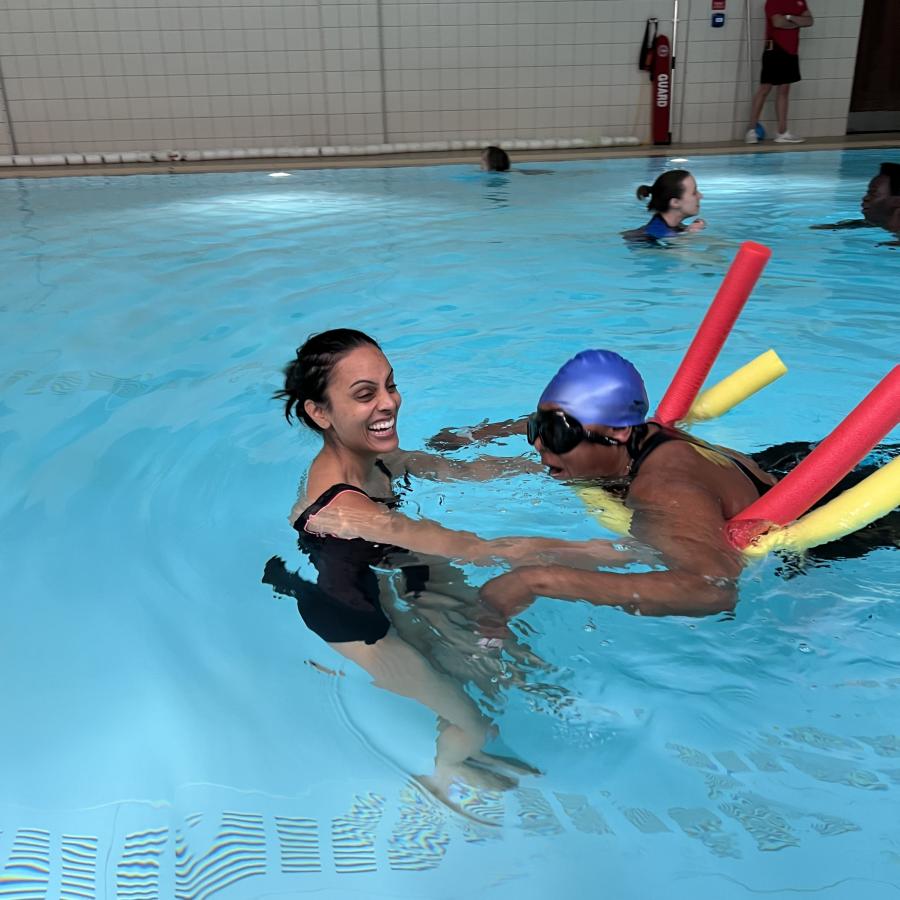 swim teacher with swimmer with blue swimming cap, coloured noodles &