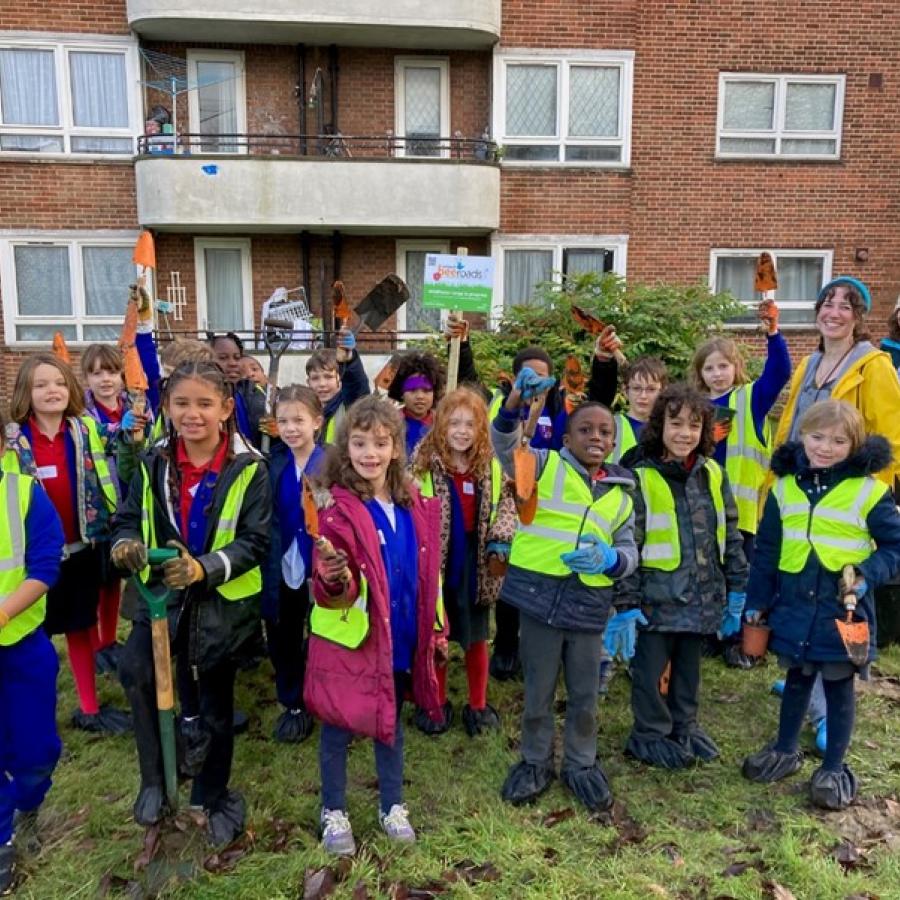 Children in high vis jackets holding gardening tools on an estate
