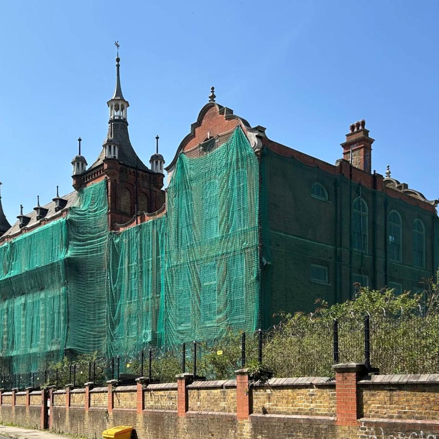 Historic building wrapped in scaffolding netting during restoration beneath clear blue skies.
