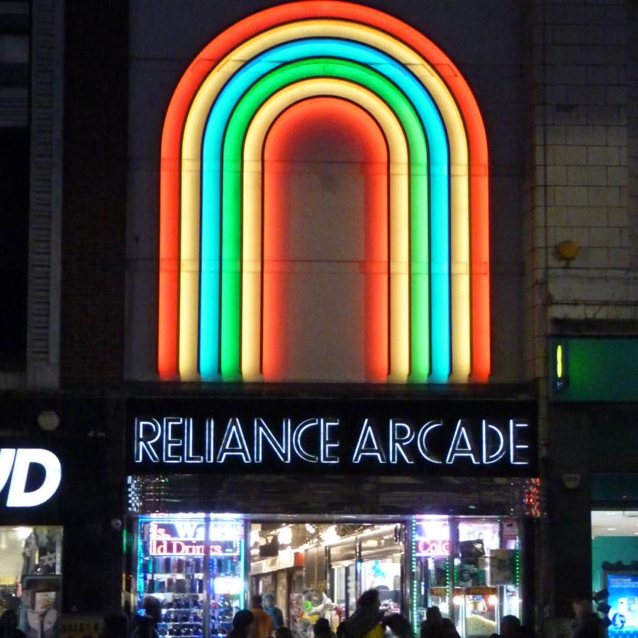Vibrant neon rainbow arches above Reliance Arcade entrance at night.