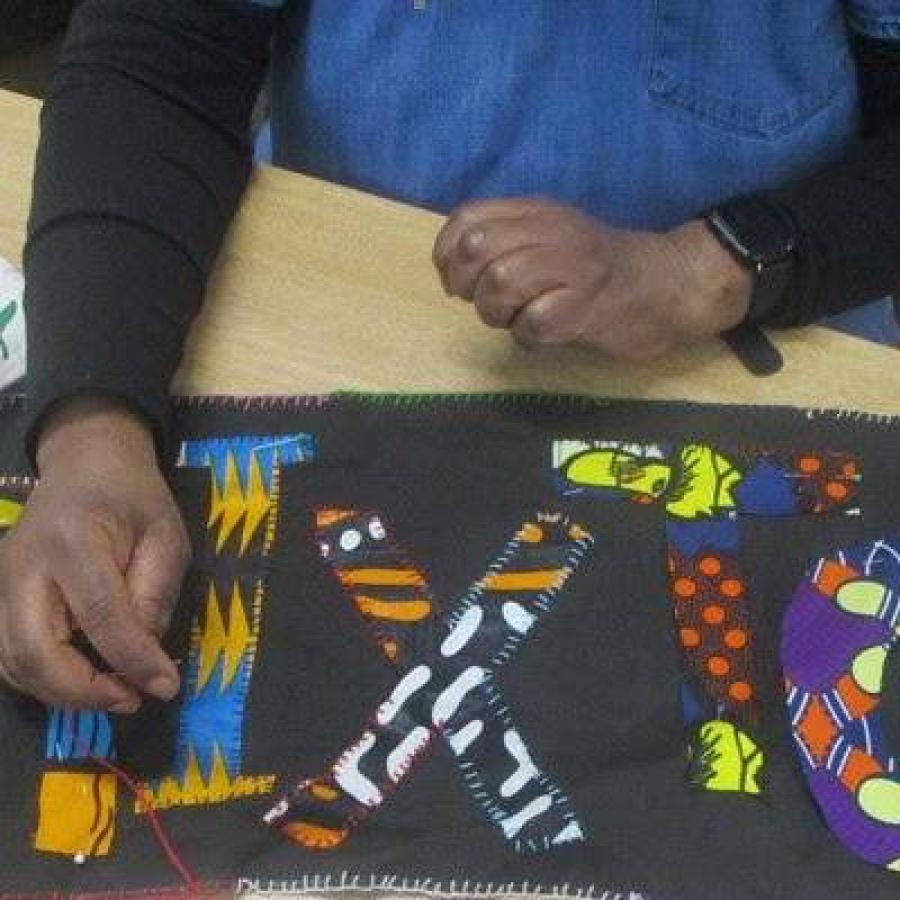 A person displaying a colourful handcrafted fabric featuring bold, patterned letter shapes.