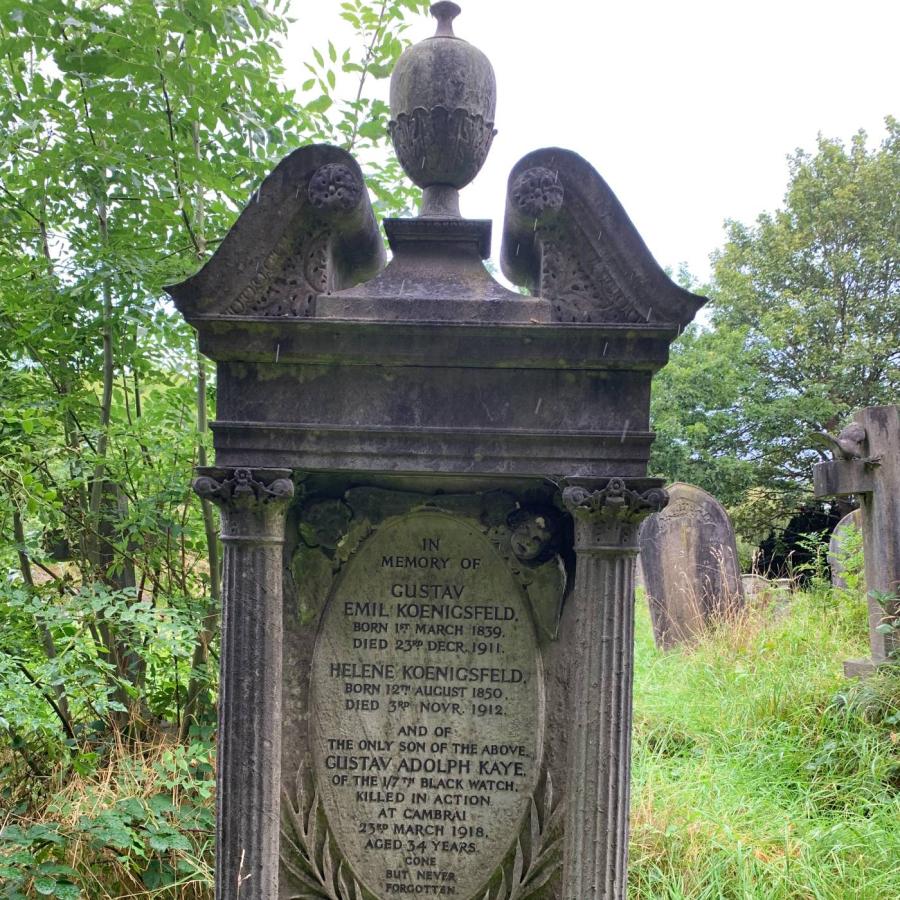 Ornate Victorian gravestone commemorating family amid overgrown cemetery with surrounding mature trees.