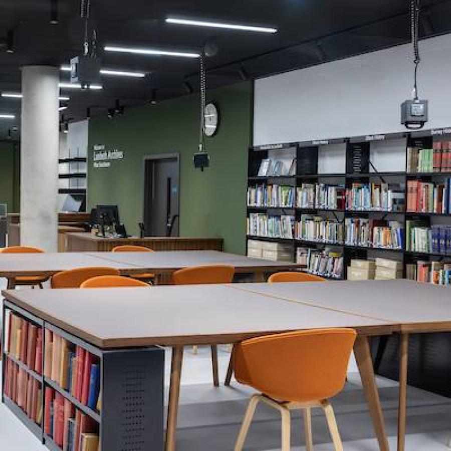 Modern library reading area with bookshelves, study tables, orange chairs