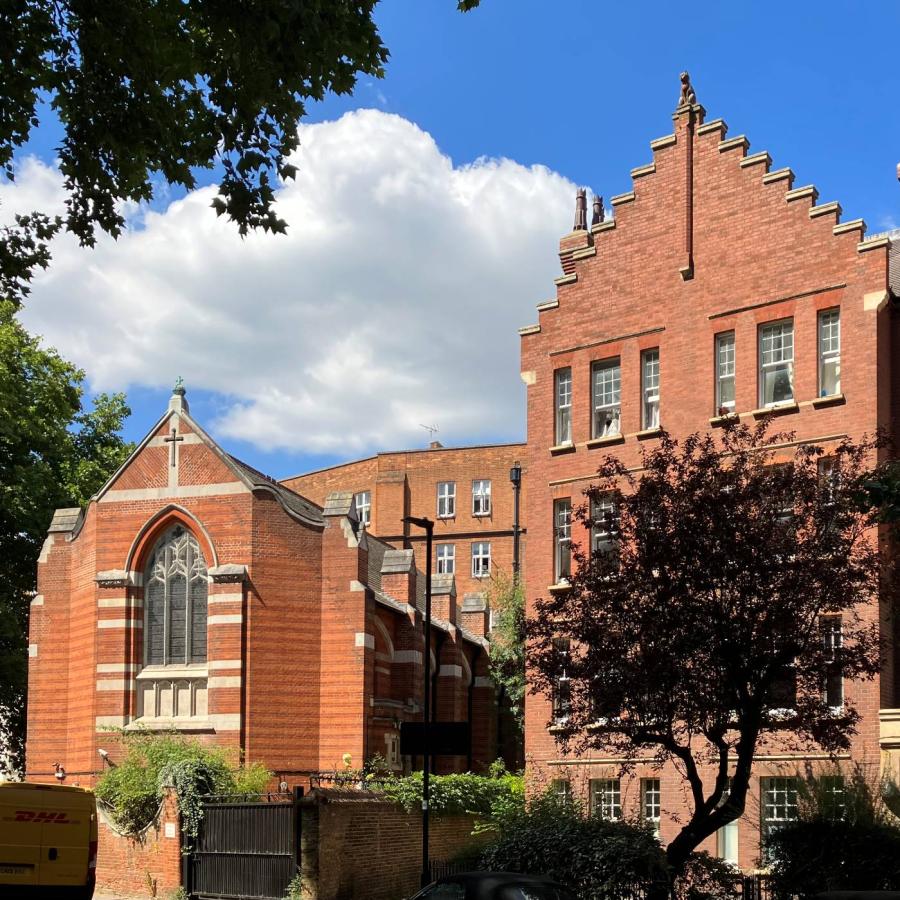 Red-brick church beside historic building beneath dramatic clouds and leafy trees.