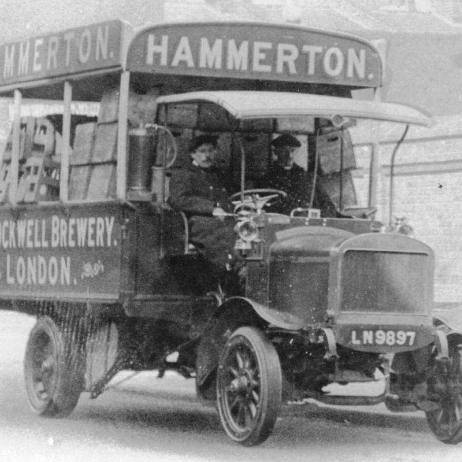 Vintage brewery delivery truck with drivers, prominent advertising, and classic design.