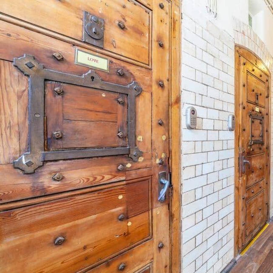 Long corridor with heavy wooden doors, tiled walls, and lighting.