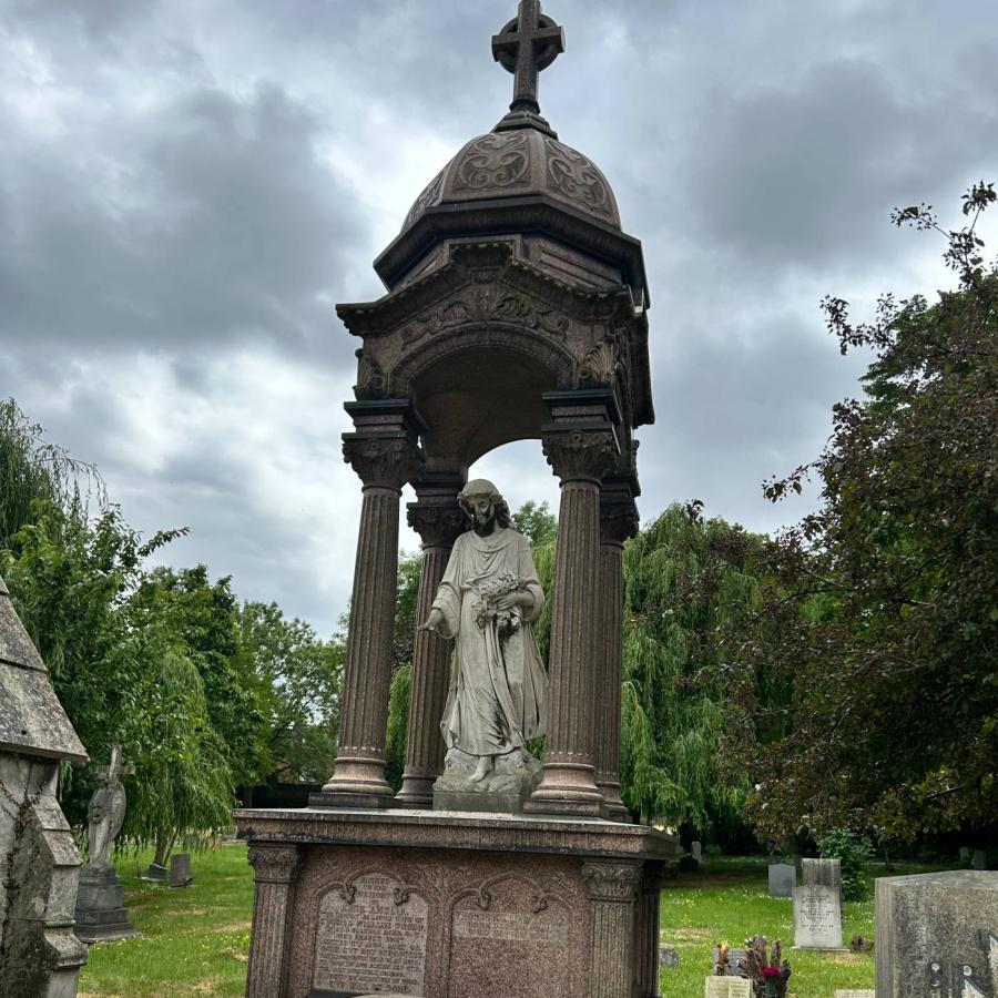 Ornate cemetery monument with statue beneath cross under stormy skies.