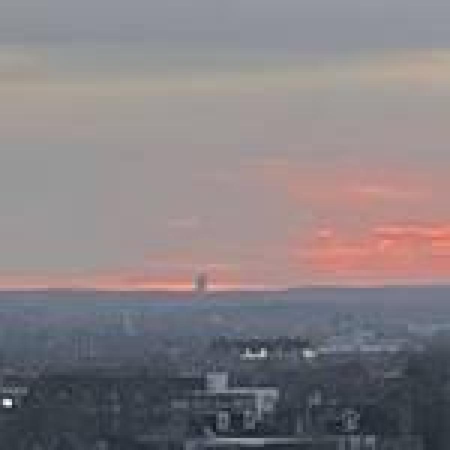 Distant plume rising above city skyline beneath colorful sunset sky.