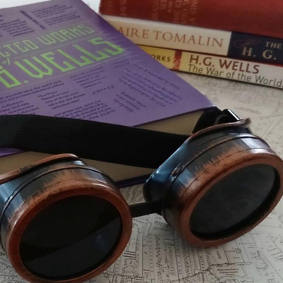 Steampunk goggles rest on map beside H.G. Wells books collection.
