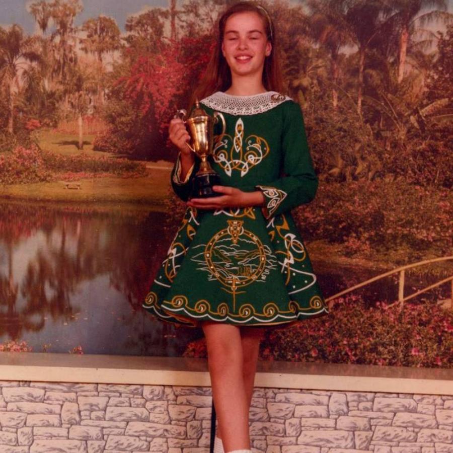 Person holding trophy wearing green embroidered dress before scenic backdrop