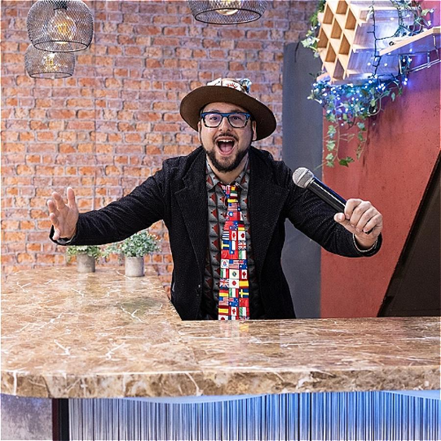 Entertainer holding a microphone, smiling and performing behind a decorated bar