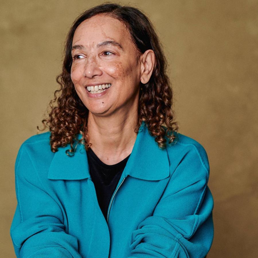 Smiling person with curly hair wearing a bright turquoise jacket.