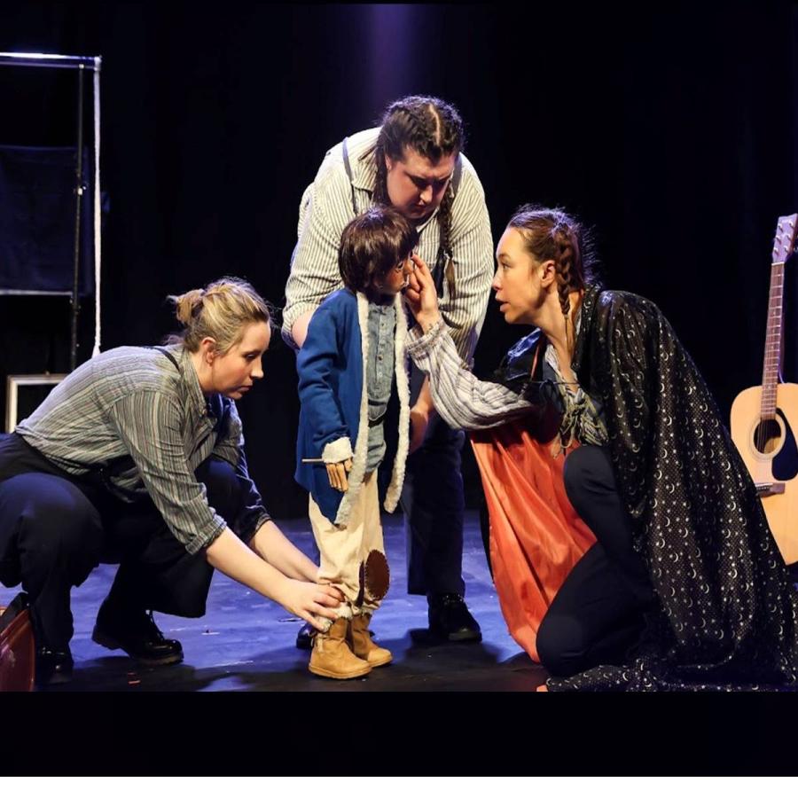 Four performers gather around a child during an intimate theatrical scene